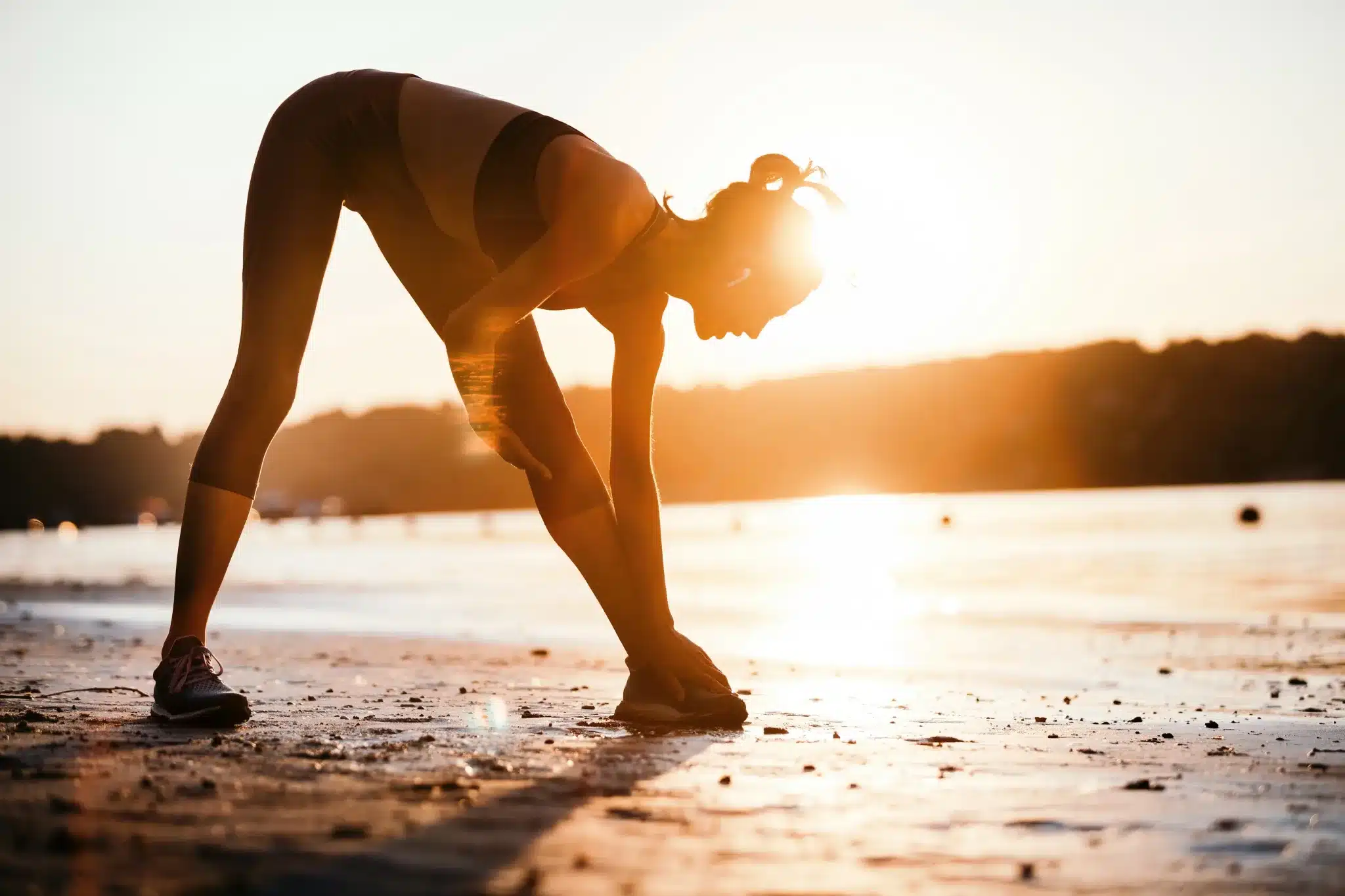 atleta femenina haciendo estiramientos y ejercicio fisico en la playa por sus beneficios para la salud