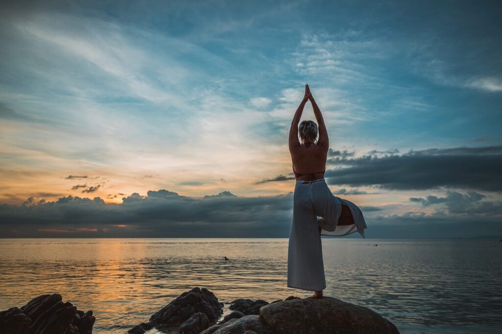 Mujer haciendo yoga sobre una roca frente al mar.