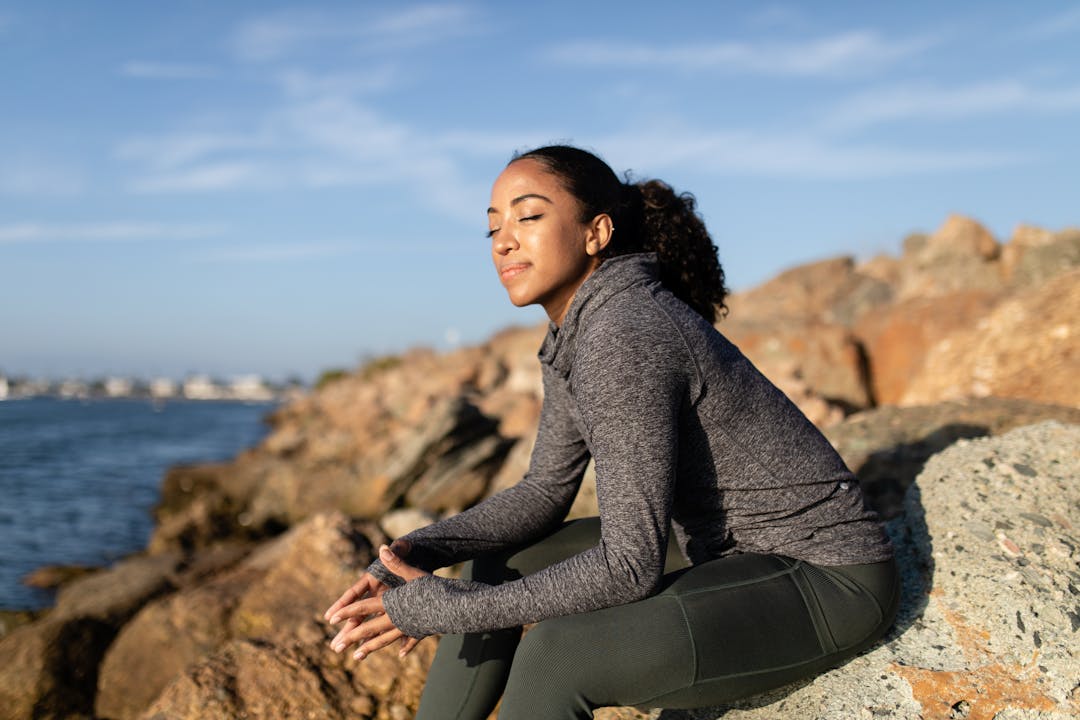 Mujer autocuidándose, respirando profundamente, sentada frente al mar.