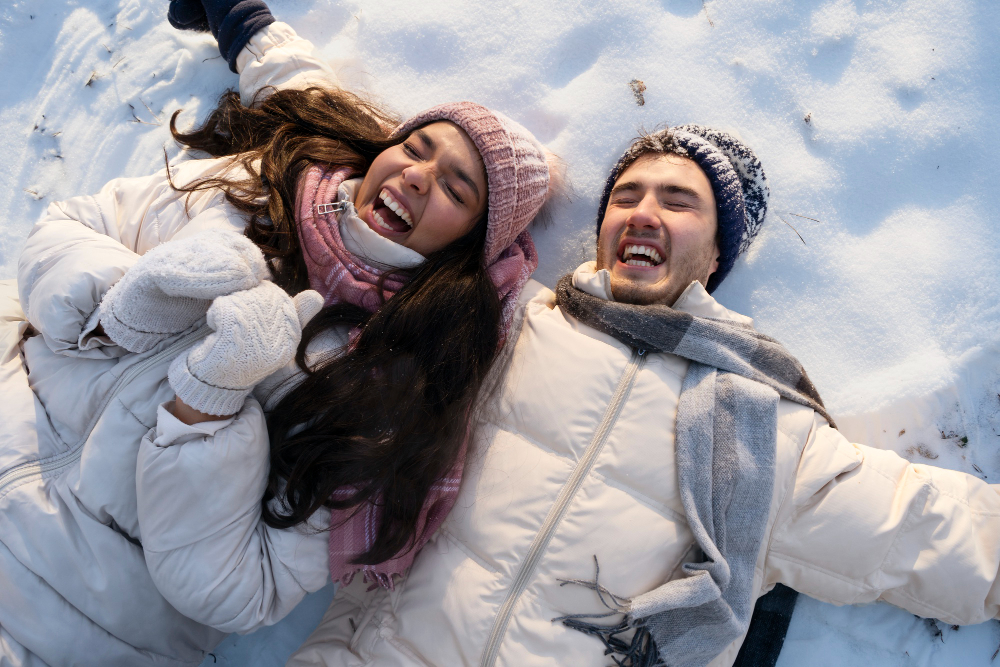 Pareja tumbada en la nieve y bien abrigada para prevenir resfriados.
